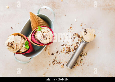 Creamy  ice cream in wafer cones served in vintage metal bowl with spoon over rustic surface.  Top view, blank space Stock Photo