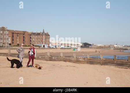 Portobello beach, Edinburgh, UK. 5th May, 2017. Two women standing with coffe. With dogs around playning on the sandy beach of Portobello, Edinburgh, Scotland, UK. Weather: 5 May 2017 It will be a fine dry day with long sunny spells for most of the region, with just the chance of some cloud pushing in to Berwickshire and East Lothian. Warm inland, west. Moderate east winds.  Tonight Clear across Dumfries and Galloway. Some low cloud will form overnight across the Lothians and eastern Borders. Chilly inland with a touch of frost in shelter. Credit: Gabriela Antosova/Alamy Live News Stock Photo