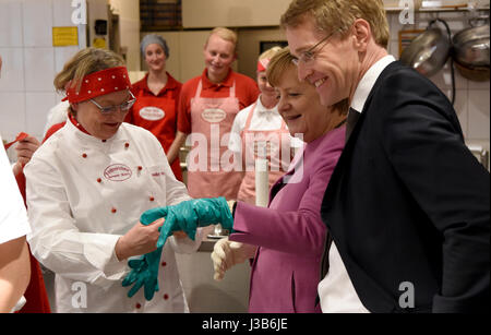 Eckernforde, Germany. 05th May, 2017. German Chancellor Angela Merkel has safety gloves put on her hands at a candy factory before a CDU campaign event in in Eckernforde, Germany, 05 May 2017. To her right stands the CDU's lead candidate for the 07 May Landtag (state parliament) election, Daniel Gunther. Photo: Carsten Rehder/dpa/Alamy Live News Stock Photo