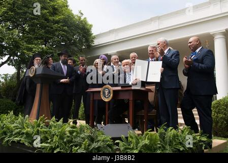 U.S. President Donald Trump holds up the signed Executive Order Promoting Free Speech and Religious Liberty surrounded by members of different faiths during a signing ceremony in the Rose Garden of the White House May 4, 2017 in Washington, D.C. Stock Photo