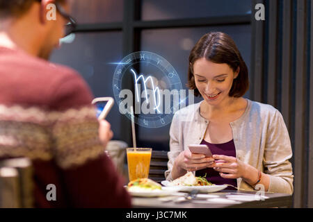 couple with smartphones and zodiac signs at cafe Stock Photo