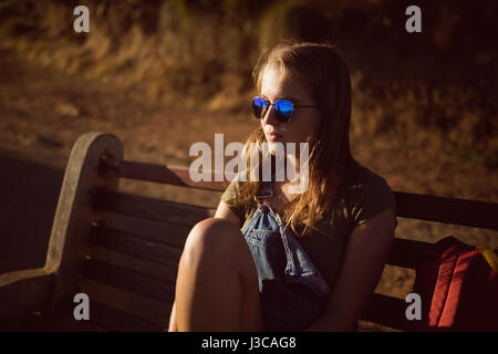 Thoughtful young woman sitting on bench in countryside Stock Photo