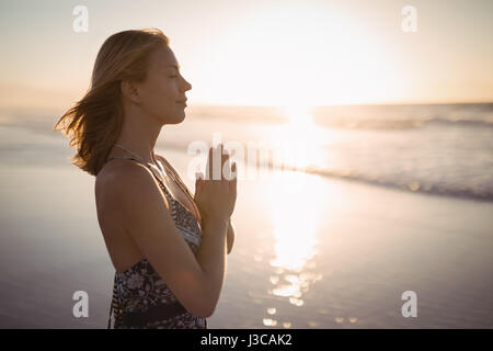 Side view of young woman doing yoga at beach during dusk Stock Photo