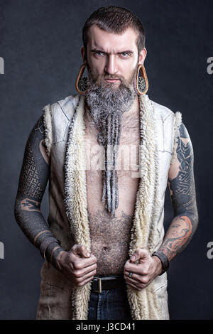 A man with a long beard and tunnels in the ears with tattoos. Stock Photo