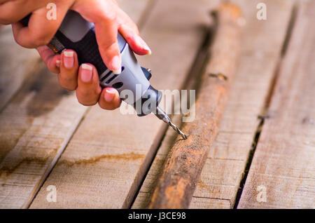 A closeup of a hardworker man drilling a wood stick with his drill on a wooden background Stock Photo