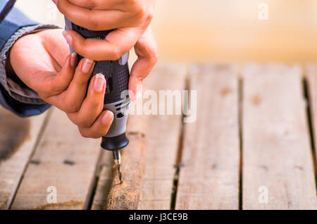 A closeup of a hardworker man drilling a wood stick with his drill on a wooden background Stock Photo