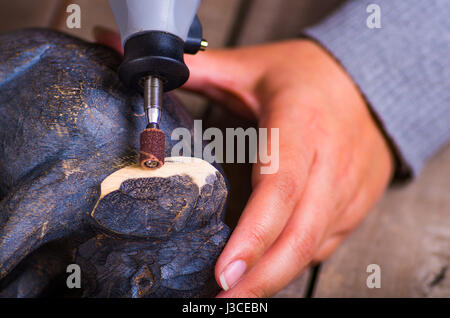 A closeup of a hardworker man using a polisher over a wood elephant on a wooden background Stock Photo