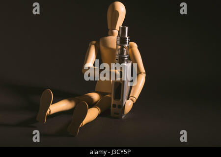 isolated wooden dummy sitting beside an electronic cigarette or vaping device. isolated on a dark background. Stock Photo