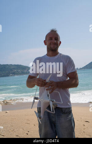 Happy man with drone camera in his hands standing on the beach over beautiful sea and sky background Stock Photo