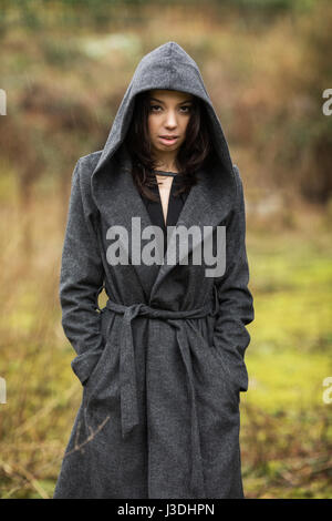 A young woman walking in the countryside dressed in a hooded coat Stock Photo