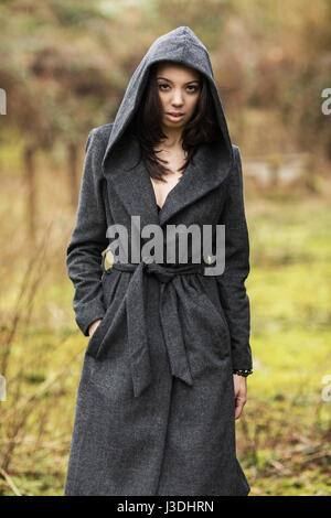 A young woman walking in the countryside dressed in a hooded coat Stock Photo