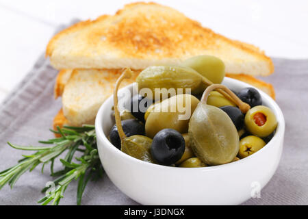 bowl of pickled olives, capers and caper berries with toast Stock Photo