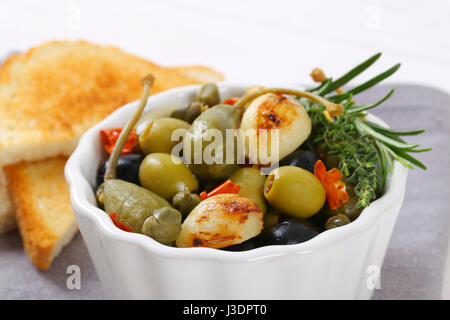 bowl of pickled olives, capers and caper berries served with toast Stock Photo