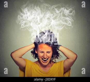 Portrait young stressed woman screaming frustrated thinking too hard steam coming out up of head isolated on grey wall background. Human face expressi Stock Photo