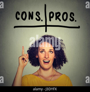 pros and cons, for and against argument concept. Young business woman with glasses looking up deciding isolated on gray wall background. Face expressi Stock Photo