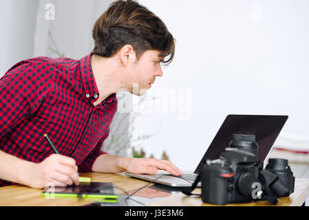 Young cute guy working in an office with a laptop and editing photos using a graphic tablet Stock Photo