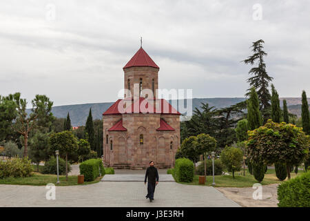 Monk walking in the grounds of the Sameba Cathedral with a small chapel in the background, in Tbilisi, Georgia. Stock Photo