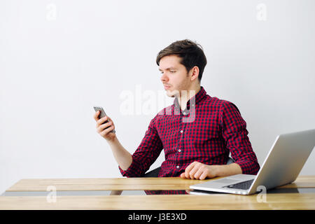 Man is reading a message on a smartphone sitting at a table in the office and smiling Stock Photo
