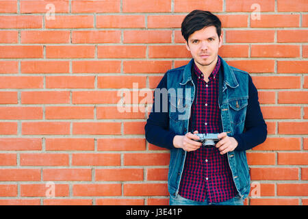 Young and handsome guy stands by a brick wall and takes pictures on a mirrorless camera Stock Photo