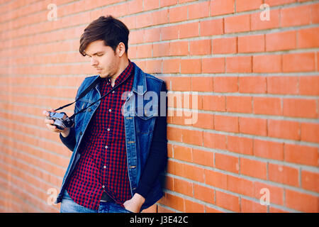 Young and handsome guy stands by a brick wall and takes pictures on a mirrorless camera Stock Photo