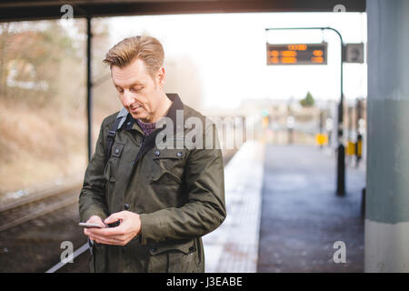 Man at a train station using his smartphone while he waits for his train. Stock Photo