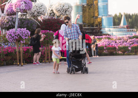 young mother and cute little girl with baby stroller walking in the flower garden Stock Photo