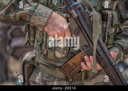 The soldier in camouflage and protective gloves, holding a gun. The zone of military operations. Stock Photo