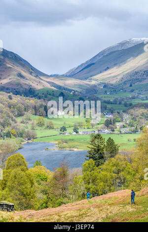 A couple of ramblers descend a hill to the lake on a sunny day in springtime at Grasmere,  lake district, Cumbria, England. Stock Photo
