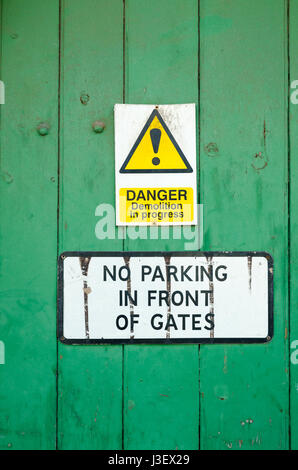 Green wooden door with signs saying no parking in front of these gates and danger demolition in progress
