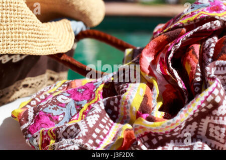Close-up of sarong beside a sun hat and a beach bag, with a swimming pool in background Stock Photo