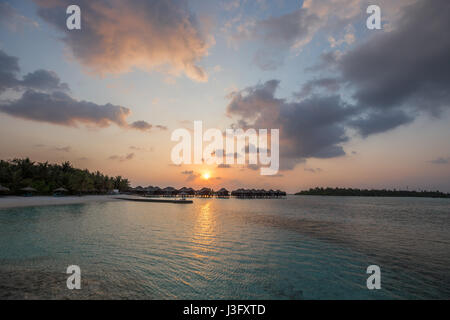Tropical Paradise Sunset Sunrise View of Over Water Bungalows with Orange Red Sky Stock Photo