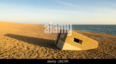 The remains of a World War II concrete pill box largely burried in the pebbles where it has slid down Chesil Beach on Dorset's Jurassic Coast. Stock Photo