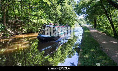 Shipley, England - June 30, 2015: A traditional narrowboat passes through the shade of woodland along the Leeds and Liverpool Canal at Shipley near Br Stock Photo