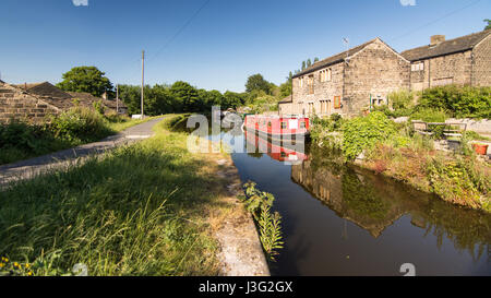 Leeds, England, UK - June 30, 2015: Narrowboats are docked alongside traditional stone houses on the Leeds and Liverpool Canal at Apperley Bridge in t Stock Photo