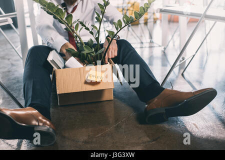 Cropped shot of young fired businessman sitting on floor with belongings in box Stock Photo