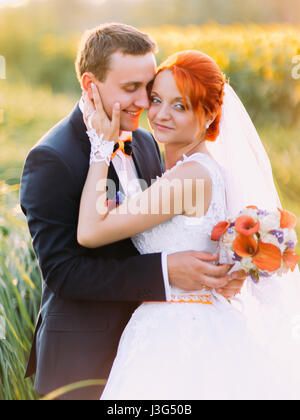 Redhair bride and stylish handsome groom posing in a sunflower sunny field. Wedding concept Stock Photo