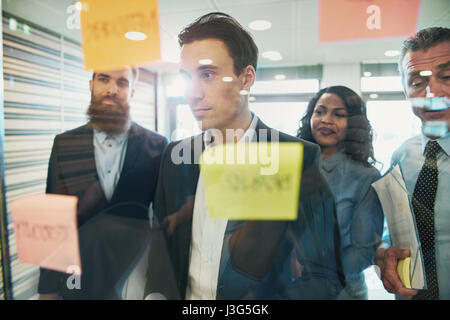 Young business team in a brainstorming meeting standing grouped around sticky memos on glass with new ideas, solutions or innovation Stock Photo