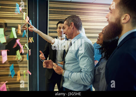 Side view of business team looking at sticky notes on glass in office Stock Photo