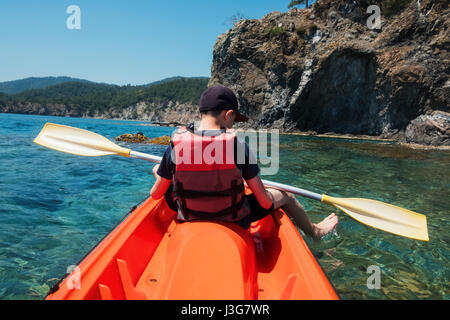 Boy in life jacket on orange kayak. Sunny day on mediterranean sea. Summer time Stock Photo