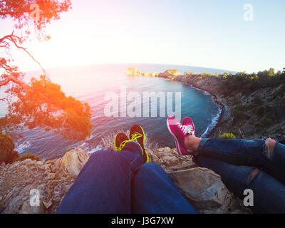 Couple legs hanging over rocks and sea bay. Amazing scene on mediterranean seacost, Summer time Stock Photo