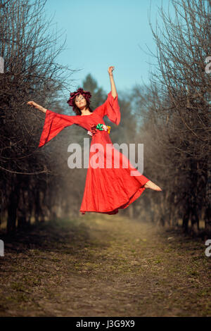 In the park among the trees levitating girl with a wreath of flowers on her head. Stock Photo