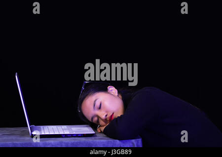 Beautiful girl fell asleep over her laptop on dark background Stock Photo