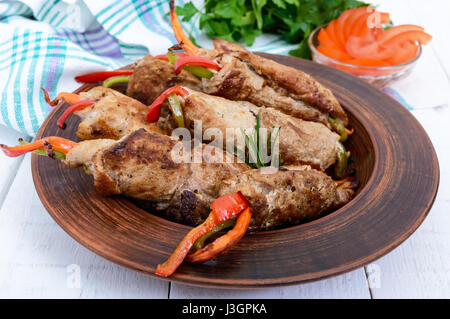 Meat rolls stuffed with sweet pepper, carrots in a clay bowl on a white wooden background. Stock Photo