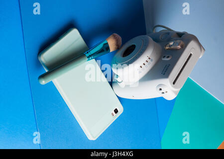 Her life on blue shades: Still Life of an instant camera, smartphone and a make-up brush placed in a multi colored blue shades Stock Photo