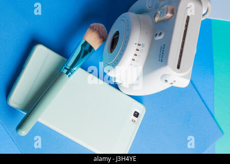 Her life on blue shades: Still Life of an instant camera, smartphone and a make-up brush placed in a multi colored blue shades Stock Photo