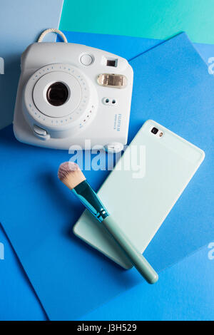 Her life on blue shades: Still Life of an instant camera, smartphone and a make-up brush placed in a multi colored blue shades Stock Photo