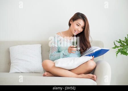 Pretty young asian woman drinking green fresh vegetable juice or smoothie from glass at home Stock Photo