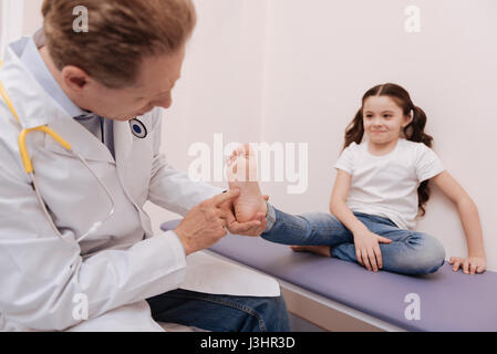 Special test. Pleasant focused capable rheumatologist running a checkup on girls reflexes while conducting a test working on her diagnosis Stock Photo