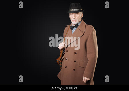 Retro style. Handsome bearded grey-haired man holding his bag on the right shoulder looking straight at camera while posing on black background Stock Photo