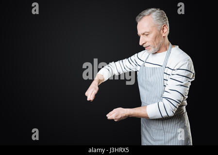 Lets cook something. Side view photo of senior male person wrinkling his forehead keeping hands in air while standing against black background Stock Photo